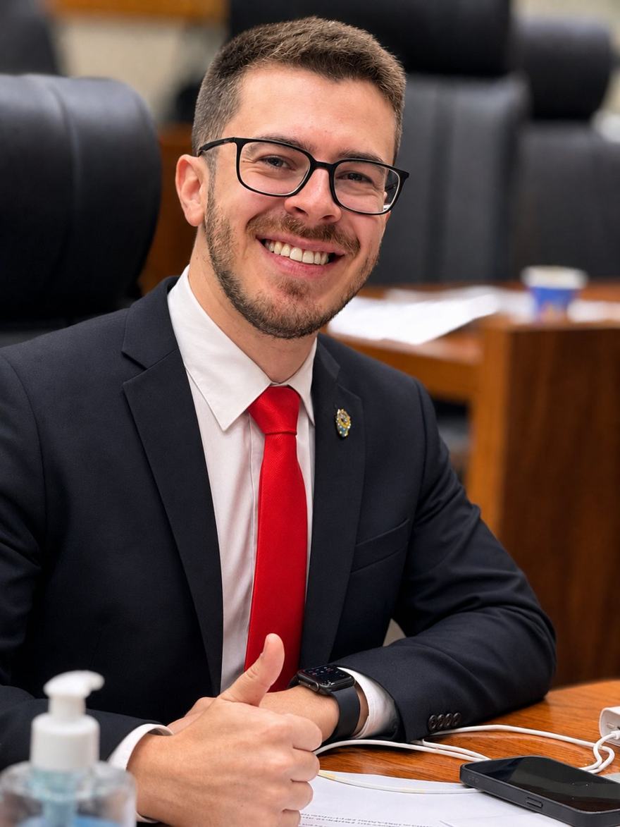 Matheus Schilling sorrindo, de terno e gravata vermelha, na Câmara Municipal